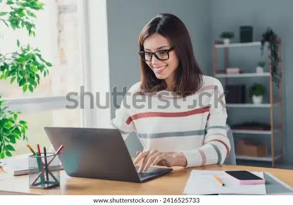 Lächelnde Frau mit Brille arbeitet an einem Laptop